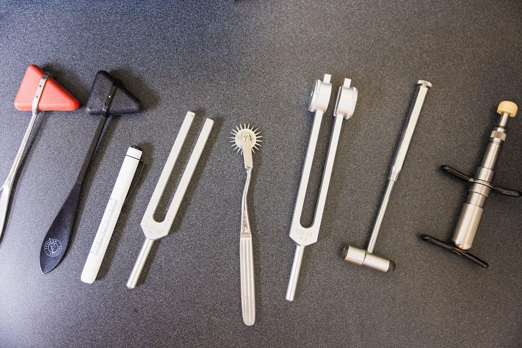 Neurological examination instruments, tuning forks, reflex hammers, and an adjusting tool arranged on a dark surface.