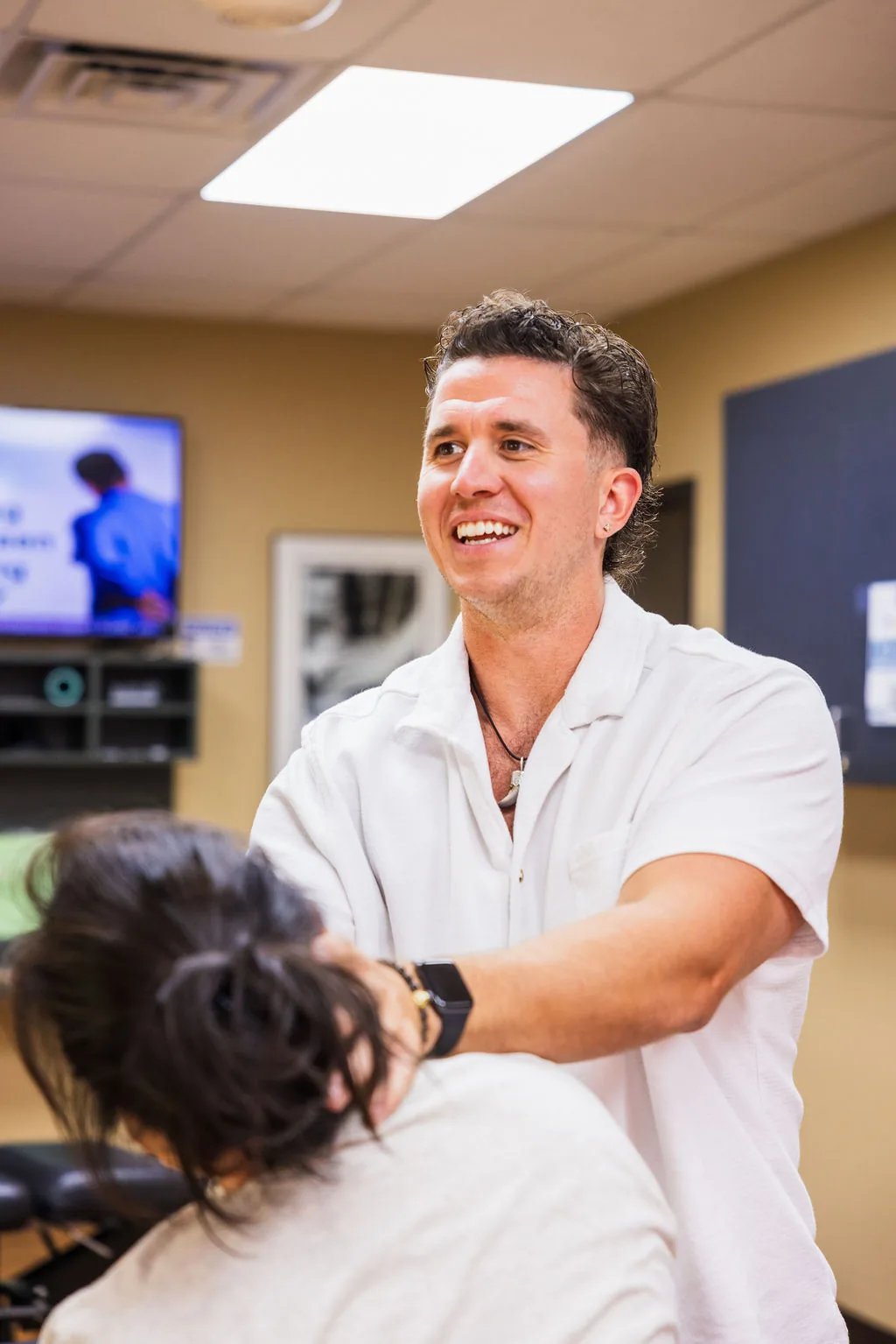 Dr. Levi Hansen smiles while performing a seated cervical neck adjustment on a patient.