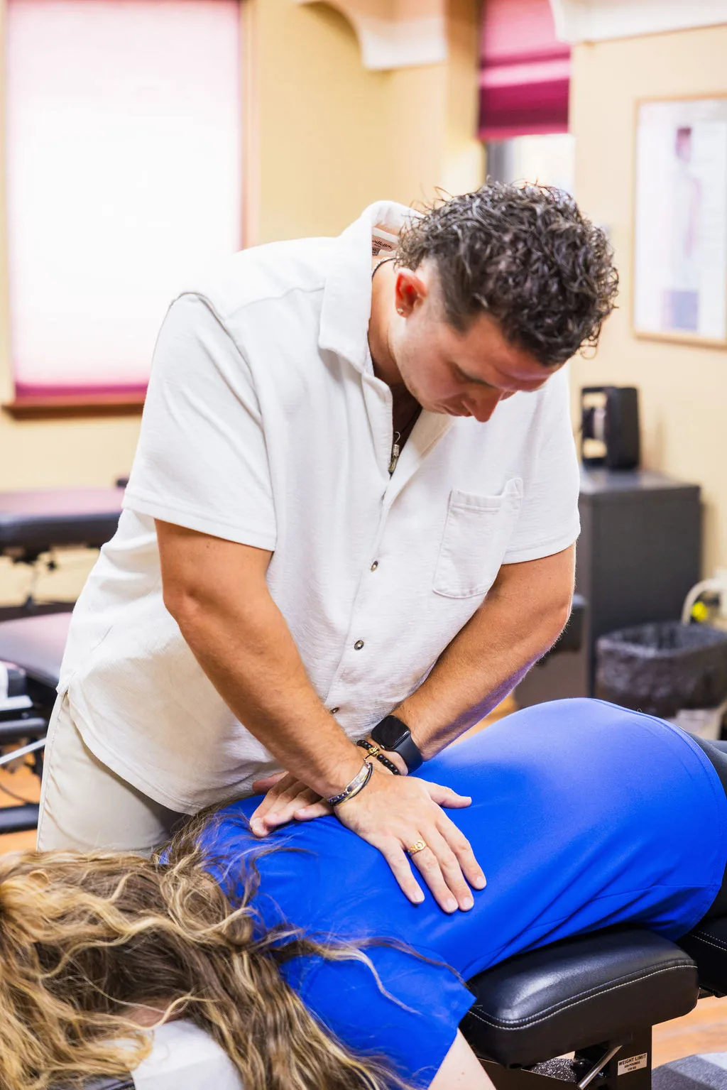 Dr. Levi Hansen performs a hands-on spinal adjustment on a patient lying prone on a chiropractic table.