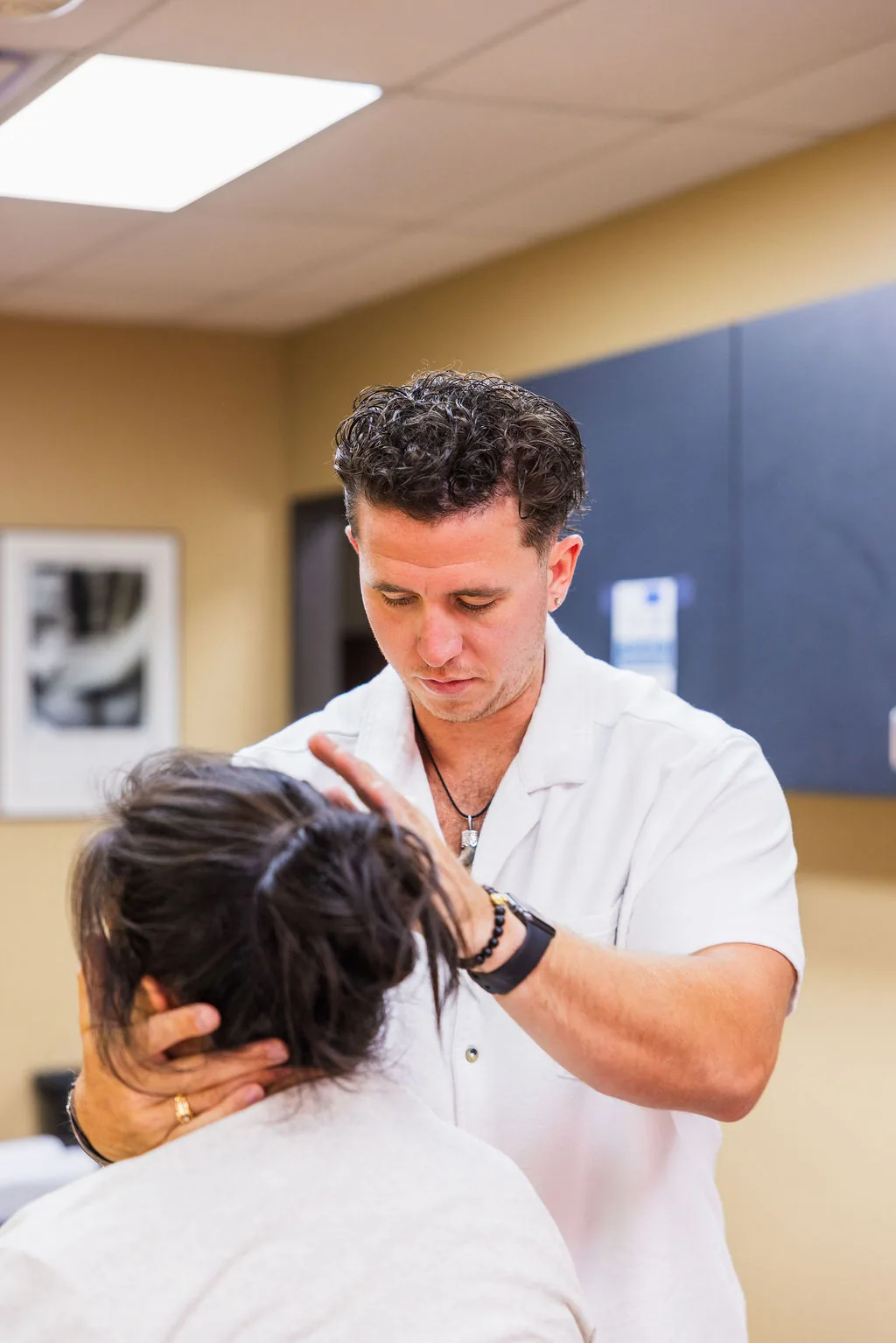 Dr. Levi Hansen examines a patient's neck and head during a chiropractic assessment in a clinic room.