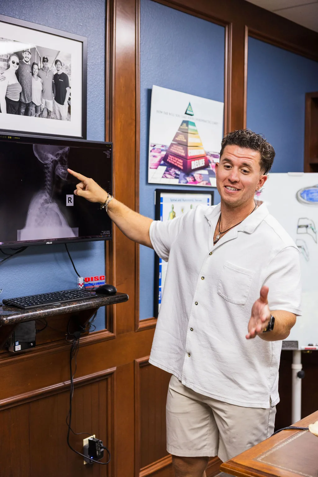 Dr. Levi Hansen points to a cervical spine X-ray displayed on an office monitor while speaking.