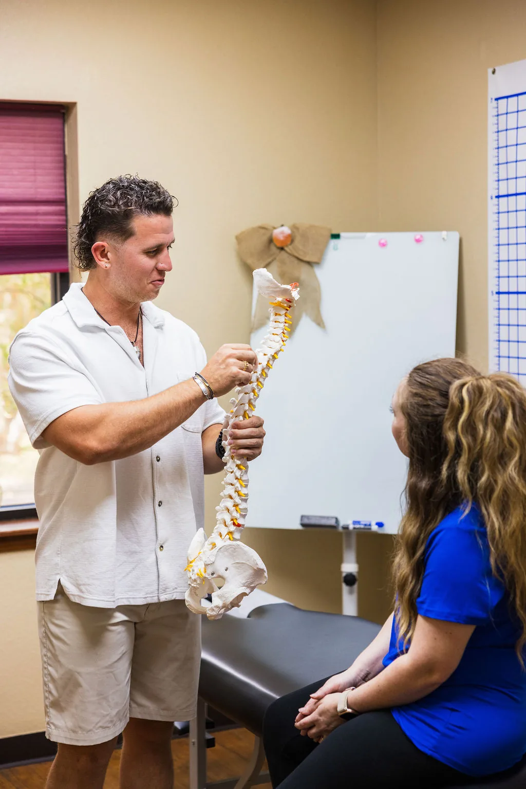 Dr. Levi Hansen holds a spine model while explaining spinal anatomy to a seated patient.