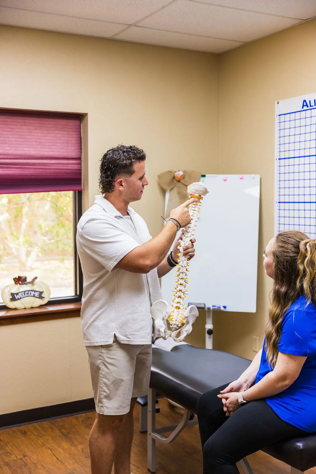 Dr. Levi Hansen holds a spine model and points to the cervical vertebrae while consulting with a seated patient.