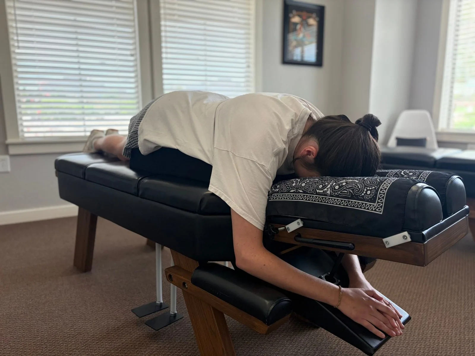 A patient rests face down on a padded chiropractic adjustment table in a bright treatment room.