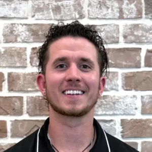 Dr. Levi Hansen smiling in a black polo shirt in front of a brick wall.