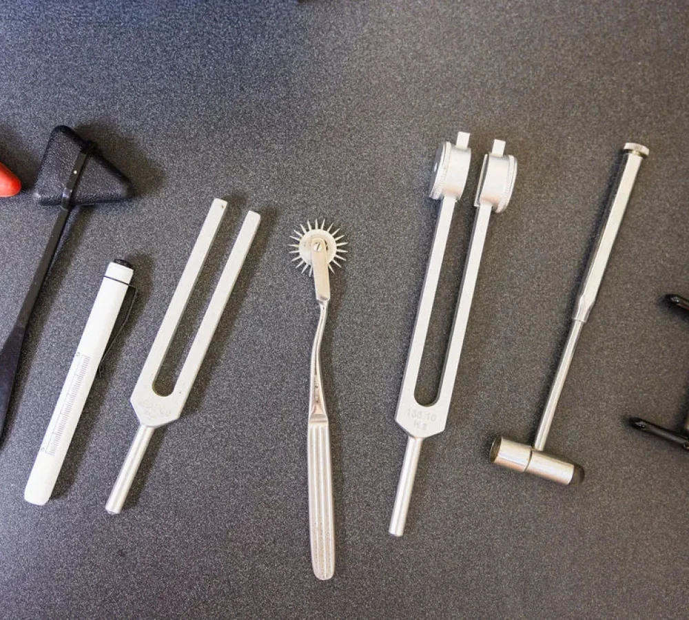 Neurological examination instruments, tuning forks, reflex hammers, and an adjusting tool arranged on a dark surface.