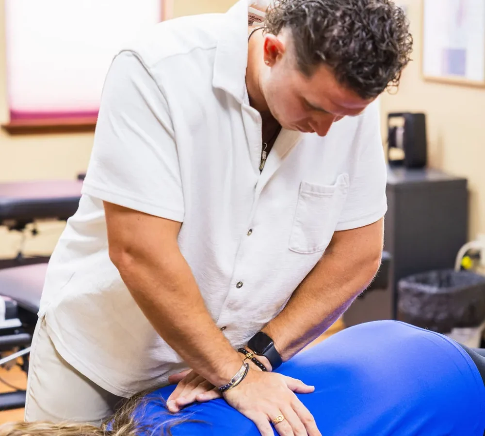 Dr. Levi Hansen performs a hands-on spinal adjustment on a patient lying prone on a chiropractic table.