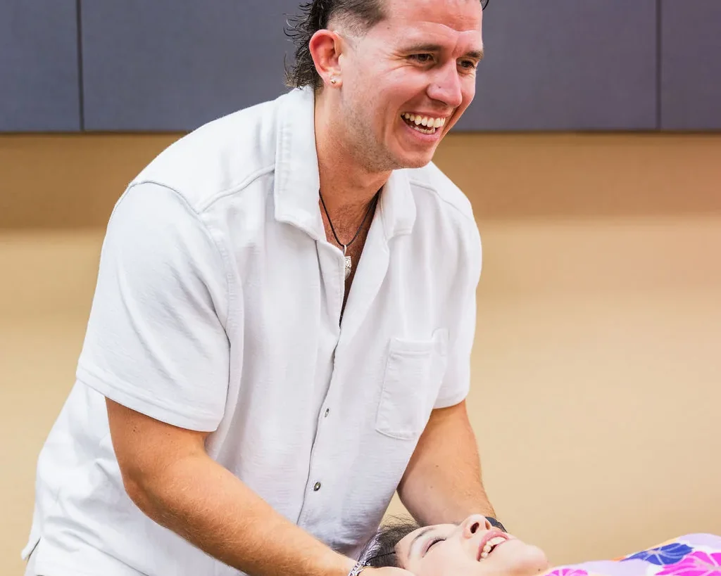Dr. Levi Hansen smiles while supporting and adjusting a patient's neck on a treatment table.