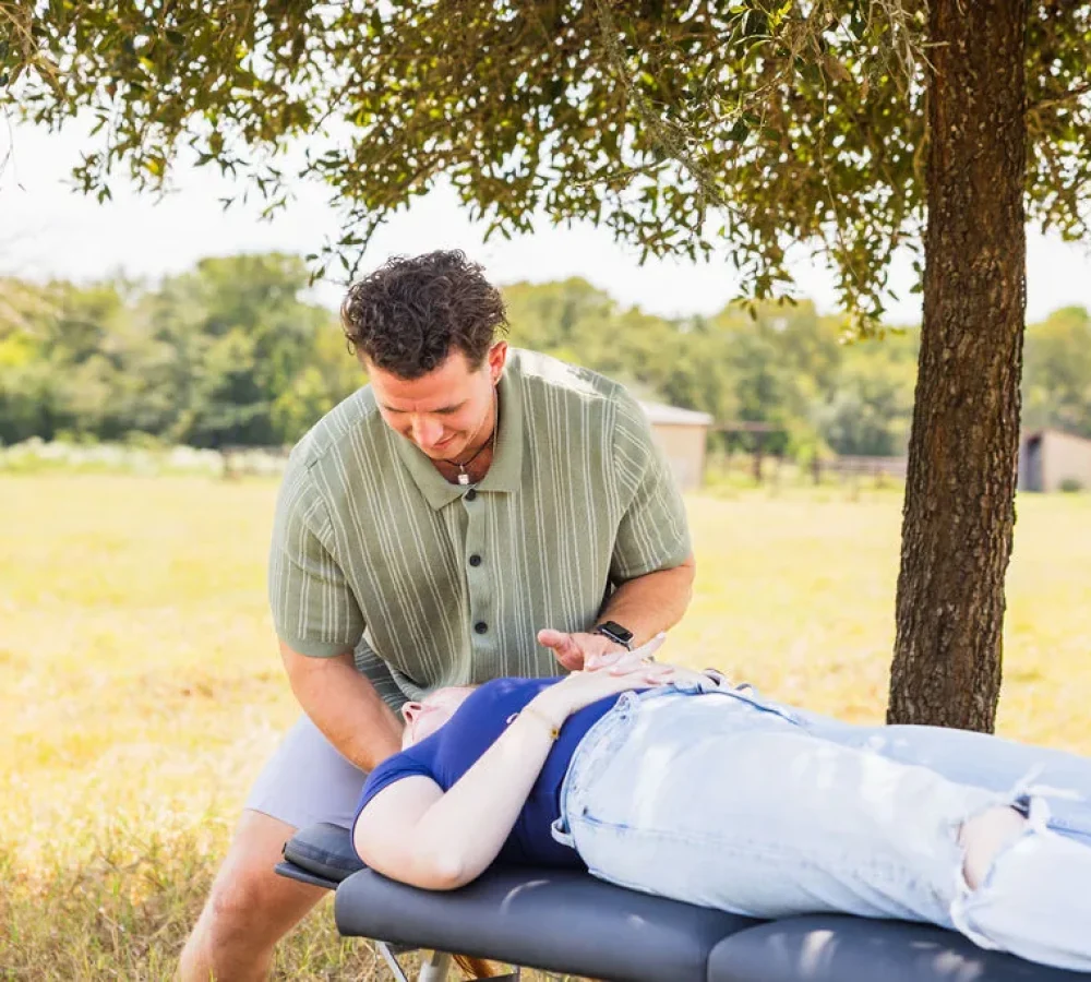 Dr. Levi Hansen assesses a patient lying on a portable adjustment table outdoors under a tree.
